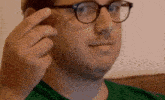 a man wearing glasses and a green shirt is holding something to his face