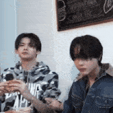 two young men are eating lobster rolls in front of a menu that says fried chicken burgers and lobster roll