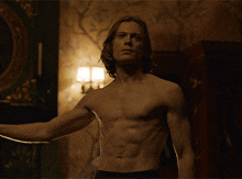 a shirtless man stands in a dark room with a lamp on the wall