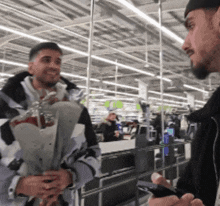 a man holding a bouquet of flowers is talking to another man in a store