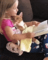 a little girl is reading a book while holding a cat on her lap