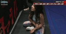 a female wrestler is sitting on the floor in front of a banner that says stardom