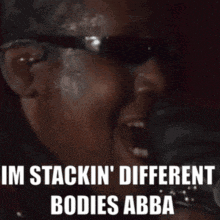 a man wearing sunglasses is singing into a microphone and says i 'm stackin ' different bodies abba .