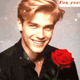 a man is smiling while holding a red rose in front of a for you banner