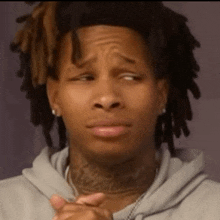 a man with dreadlocks and a tattoo on his neck is making a sad face