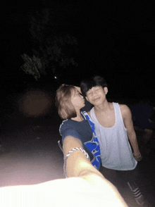 a man in a white tank top stands next to a girl in a blue shirt