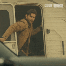 a man in a brown jacket is standing in the doorway of a trailer with countdown written on the side