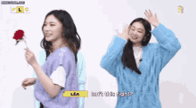 a girl in a blue sweater is standing next to another girl in a purple vest holding a red rose ..