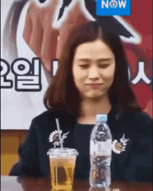a woman is sitting at a table with a cup of beer and a bottle of water