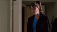 a woman wearing a blue shirt and a black coat stands in front of a door