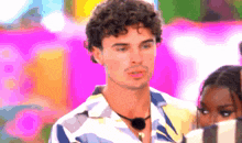 a man with curly hair is wearing a striped shirt and a black necklace .