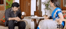 a man is sitting on a couch while a woman sits at a table .