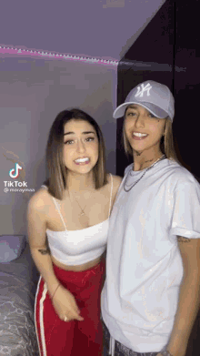 two women are standing next to each other and one has a ny hat on