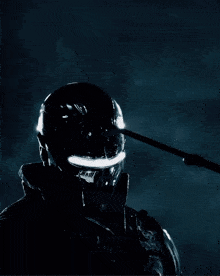 a man wearing a futuristic helmet holds a spear in front of his face