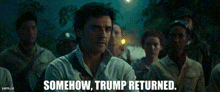 a man in a white shirt is standing in front of a group of people and says " somehow trump returned "