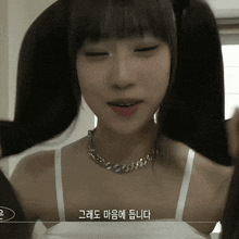 a woman wearing a white tank top and a silver necklace has korean writing on her chest