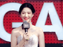 a woman in a white dress is smiling and holding a microphone in front of a sign that says bazaar gala