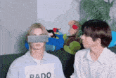 two men are sitting on a couch and one has a sign that says pado