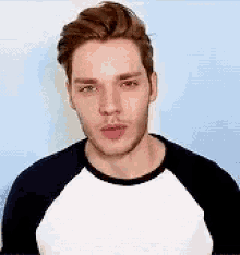 a young man with a beard is wearing a white and black shirt and making a funny face .