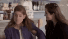 two women are talking to each other in a kitchen .