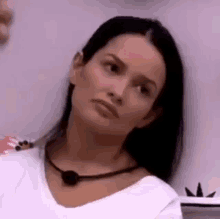 a woman wearing a white shirt and a black necklace is leaning against a wall and making a funny face .