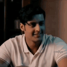 a man wearing a white polo shirt is smiling in a dark room .