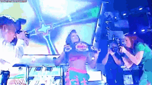 a woman is holding a wrestling championship belt on a stage while a group of people are standing around her .
