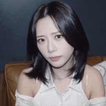 a woman with black hair and a white shirt is sitting on a brown couch