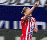 a soccer player in a red and white uniform is pointing up at the sky