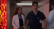 a man and a woman in scrubs are walking down a hallway .