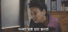 a woman in a purple vest is sitting in front of a window with a foreign language behind her