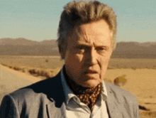 a man in a suit and scarf is standing in a desert