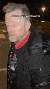 a man with a beard is wearing a black jacket and a red turtleneck sweater