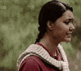 a woman wearing a red shirt and a scarf around her neck is standing in front of trees .