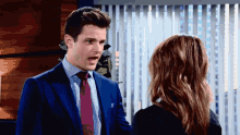 a man in a suit and tie is talking to a woman in a black shirt