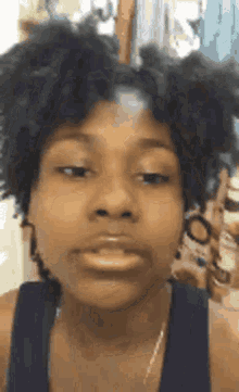 a woman with curly hair is making a funny face while wearing a blue tank top .