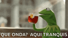 kermit the frog is holding a cup of tea and says que onda ? aqui tranquis