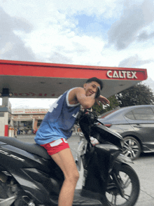 a man is riding a scooter in front of a caltex gas station