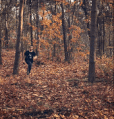 a man wearing a black shirt with a skull on it is running through a forest