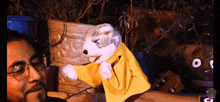 a man with glasses holds a stuffed animal with a yellow jacket on