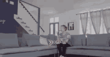 a man is sitting on a couch in a living room with stairs in the background .