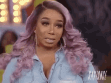 a woman with purple hair is wearing a blue denim shirt and earrings .