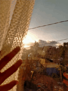 a person 's hand is reaching out through a window towards a sunset