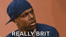 a man wearing a blue hat and a blue shirt is making a funny face and saying `` really brit '' .
