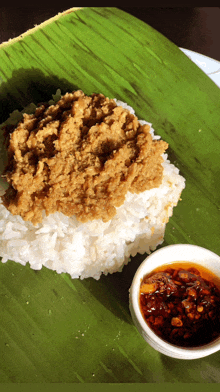 a bowl of sauce sits next to a plate of food on a banana leaf