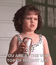 a little girl is holding a can of soda and saying `` you are at the top of my shit list '' .