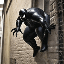 a statue of a black spiderman is climbing a brick wall