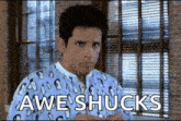a man in pajamas is standing in front of a window with the words awe shucks written on the screen .