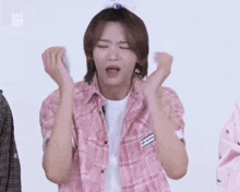 a young man in a pink plaid shirt is making a funny face with his hands .