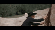 a man in a cowboy hat is climbing a rock